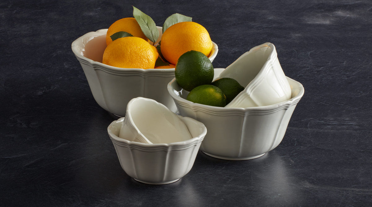 White ceramic bowls in varying sizes arranged on a dark surface, filled with lemons and limes.