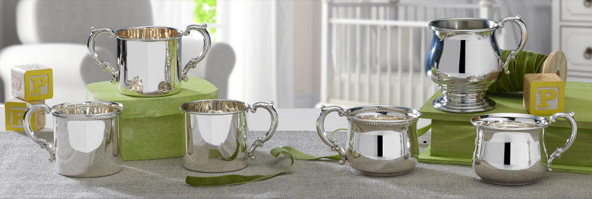 Empire Silver collection of polished silver mugs with ornate handles arranged on a table with green risers.