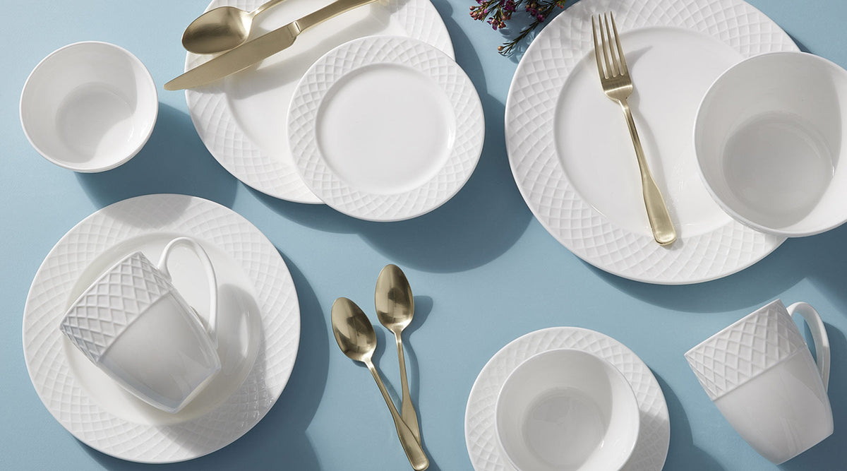 Trellis White dinnerware collection with lattice patterned plates and gold cutlery on a blue surface.