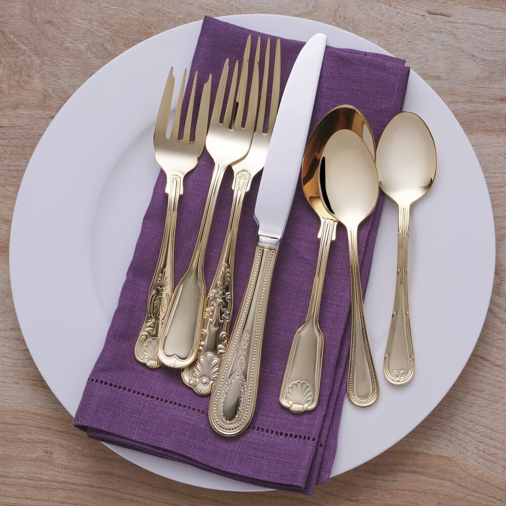 Gold plated flatware displayed on a purple napkin atop a white plate