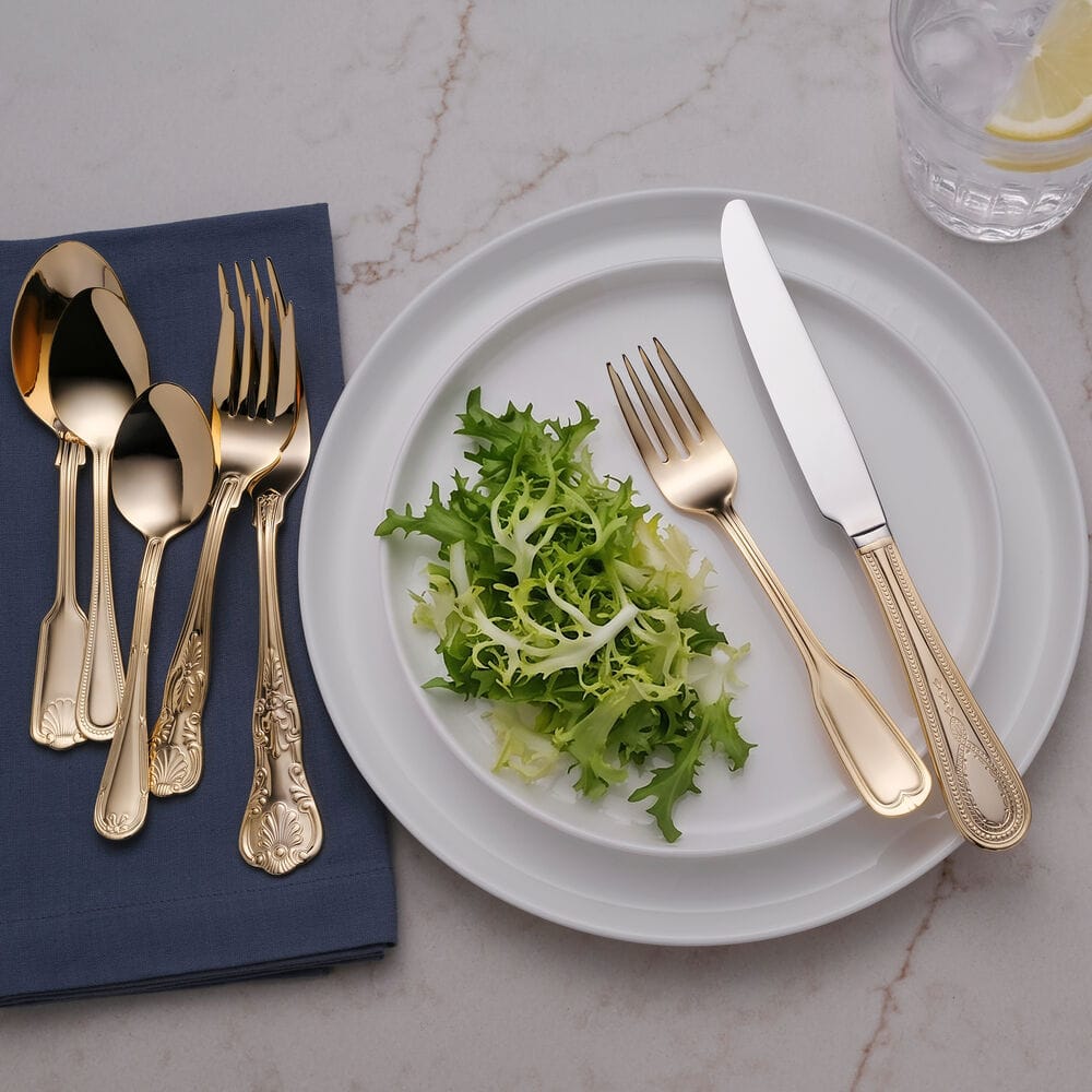 Gold plated flatware on a navy napkin beside a salad plate