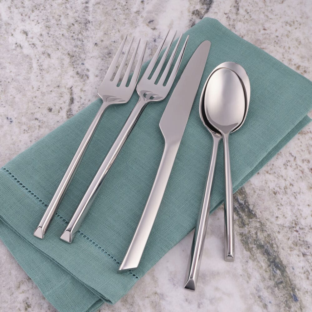 Close up of Jacqueline forged flatware neatly arranged on a teal napkin showing forks knife spoon and teaspoon