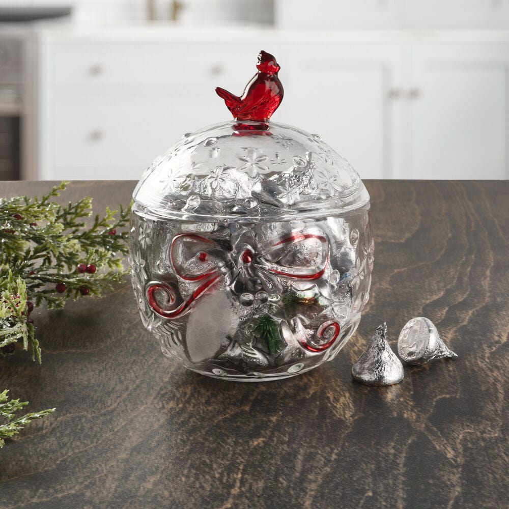 Clear glass candy box with floral patterns and a red cardinal lid topper shown on a kitchen table.