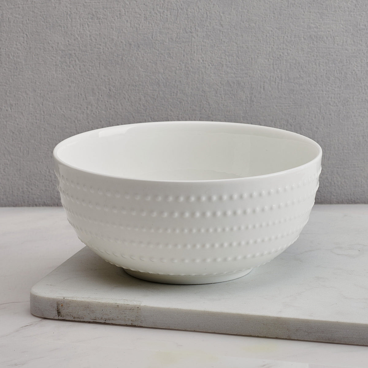 Close-up of a white Nellie soup cereal bowl with a dotted texture on a wood surface.