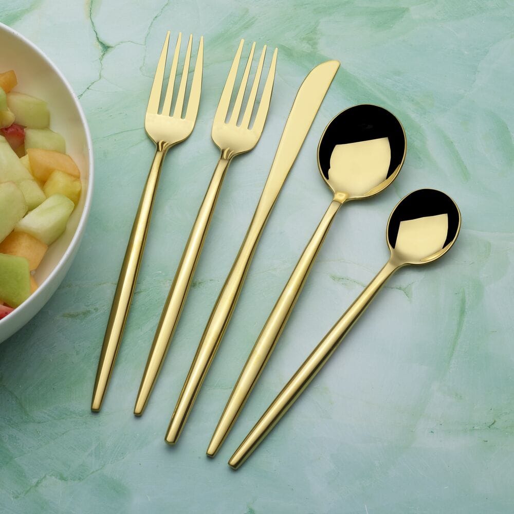 Gold plated flatware set arranged on a mint green surface with a salad bowl nearby