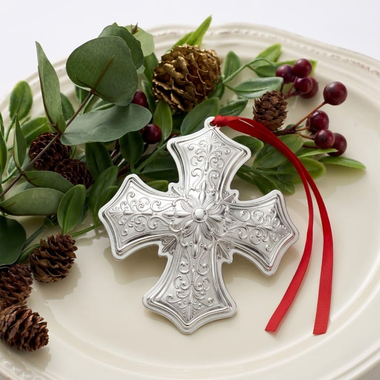 Gorham 2026 Sterling Silver Cross Ornament 13th Edition ornate cross resting on a plate with greenery and pinecones