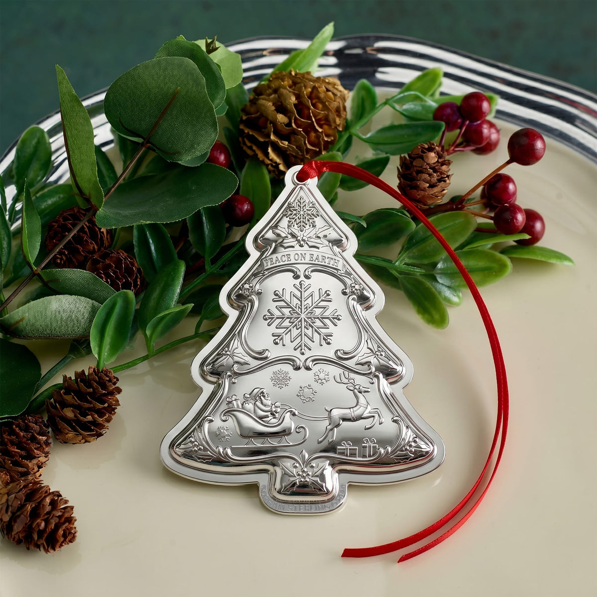 Gorham 2026 sterling silver Christmas tree ornament shown among greenery pinecones and red ribbon