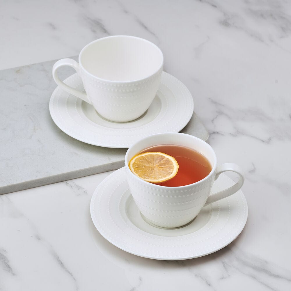 Nellie set of two white teacups with matching saucers on a marble surface, one cup containing tea with lemon slice