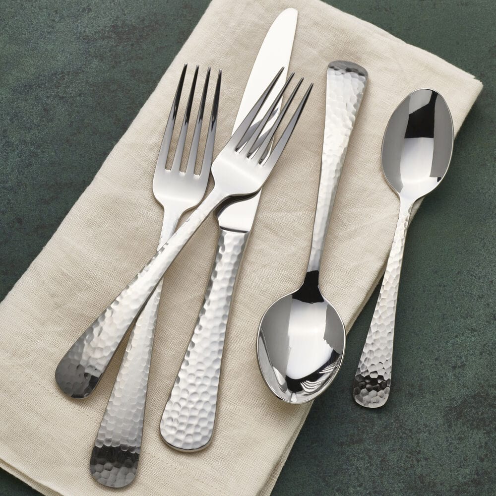 Hammered opulent flatware set displayed on a linen napkin with forks knives and spoons