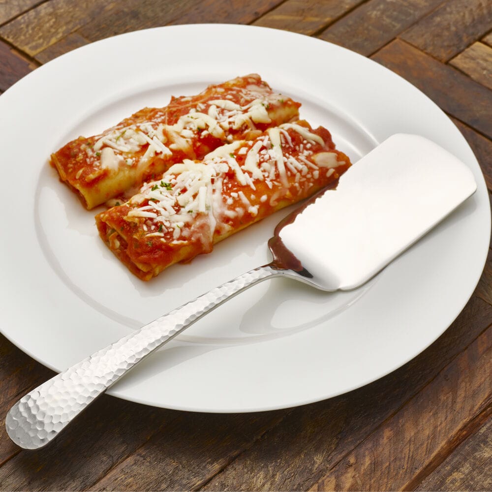Hammered opulent flatware serving spatula beside two cannelloni on a white plate