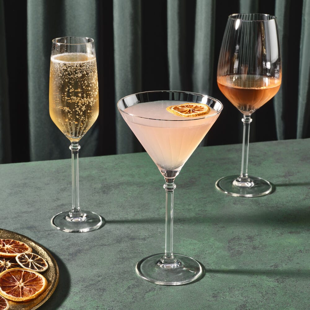 Three Eloise glassware pieces: champagne flute left, martini glass center, and another glass on the right on a green table