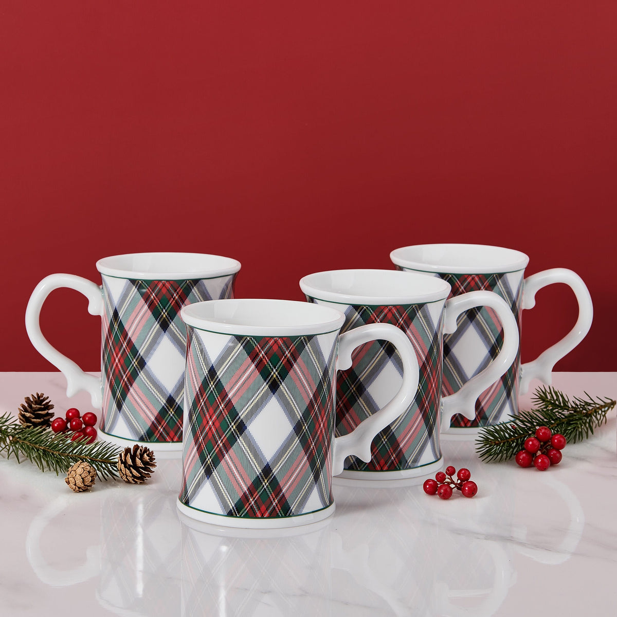 Stack of white mugs in tartan plaid pattern with festive pinecones and berries on a red backdrop