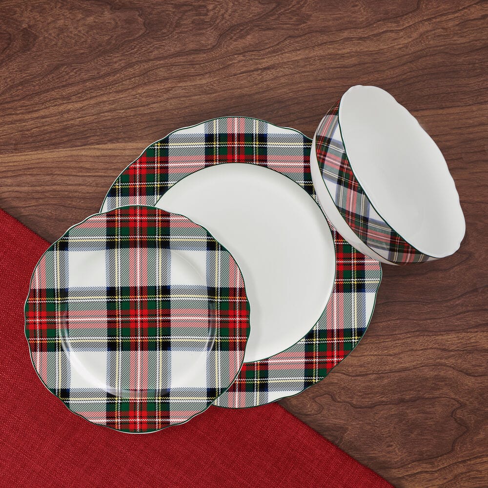 Tartan plaid scalloped edge dinnerware set for four arranged on a wood surface with a red napkin.