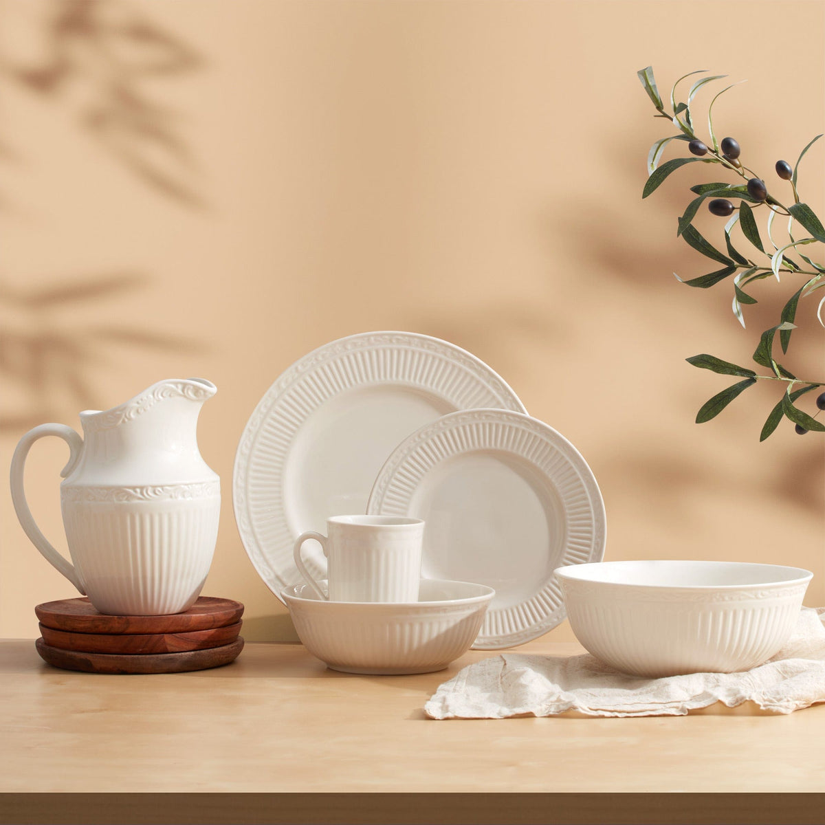 Still life of white Italian Countryside dinnerware with pitcher bowls and plates on a peach background and olive branch