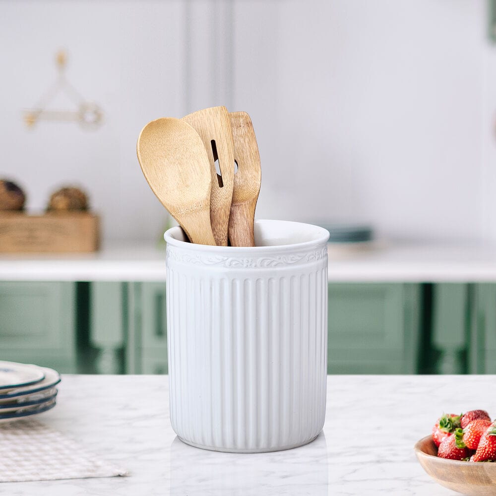 White ribbed ceramic utensil crock holding wooden cooking utensils on a marble countertop.