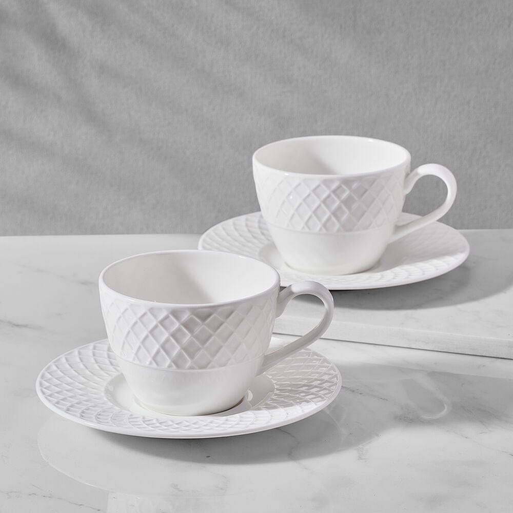 Pair of white Trellis tea cups with textured pattern and matching saucers on a marble surface.