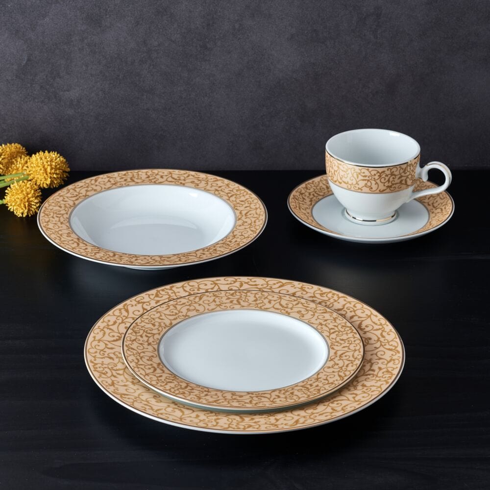 Cup and saucer with a gold scroll border beside stacked plates from the Parchment Gold dinnerware set on a dark backdrop.