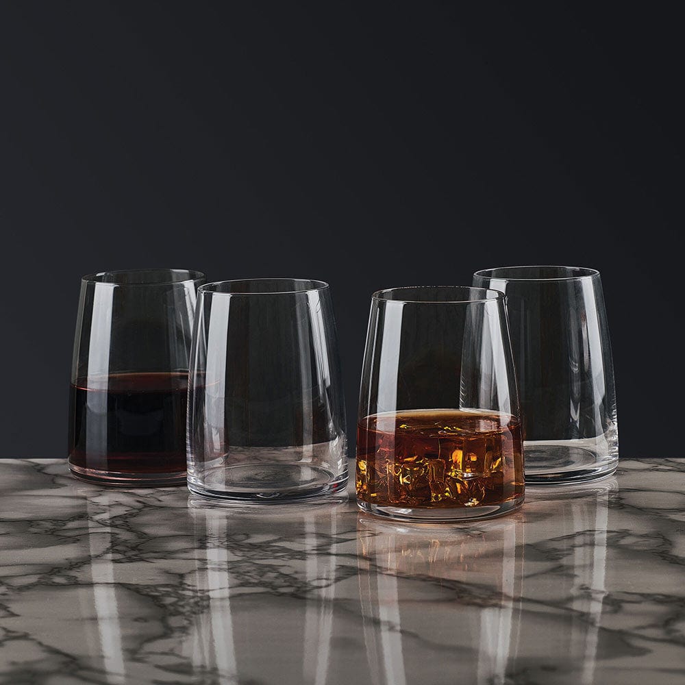 Four glassware tumblers against a dark background with the front right glass filled with whiskey and ice