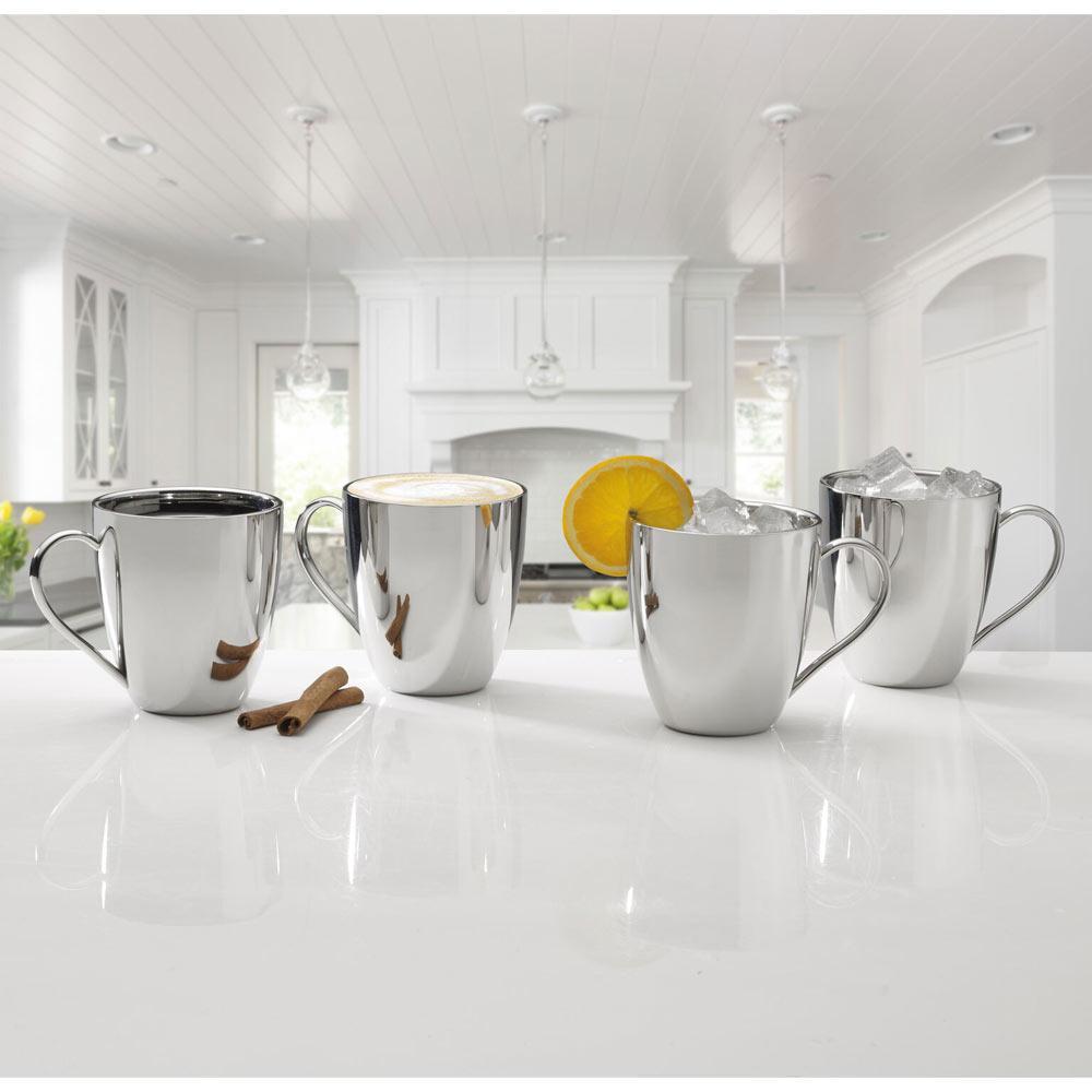 Four polished stainless steel mugs on a white kitchen island, one with an orange slice on the rim and the others filled with ice