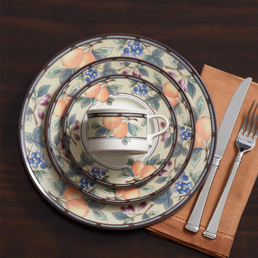 Garden Harvest place setting with stacked dinner plates a teacup and silverware on an orange napkin