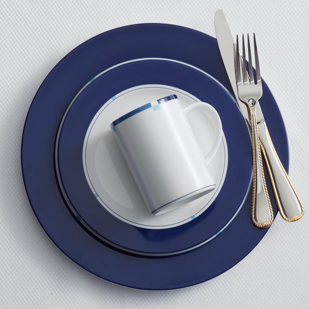 Overhead view of a Jet Set blue accent place setting with a mug on white plate inside a navy charger and silverware.