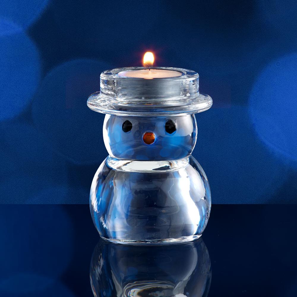 Blue glass snowman tealight holder with a lit tealight on top against a deep blue backdrop.