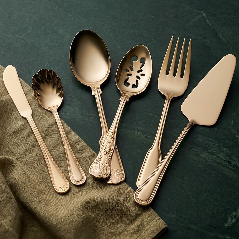 Gold plated flatware with ornate handles laid out on a dark teal surface