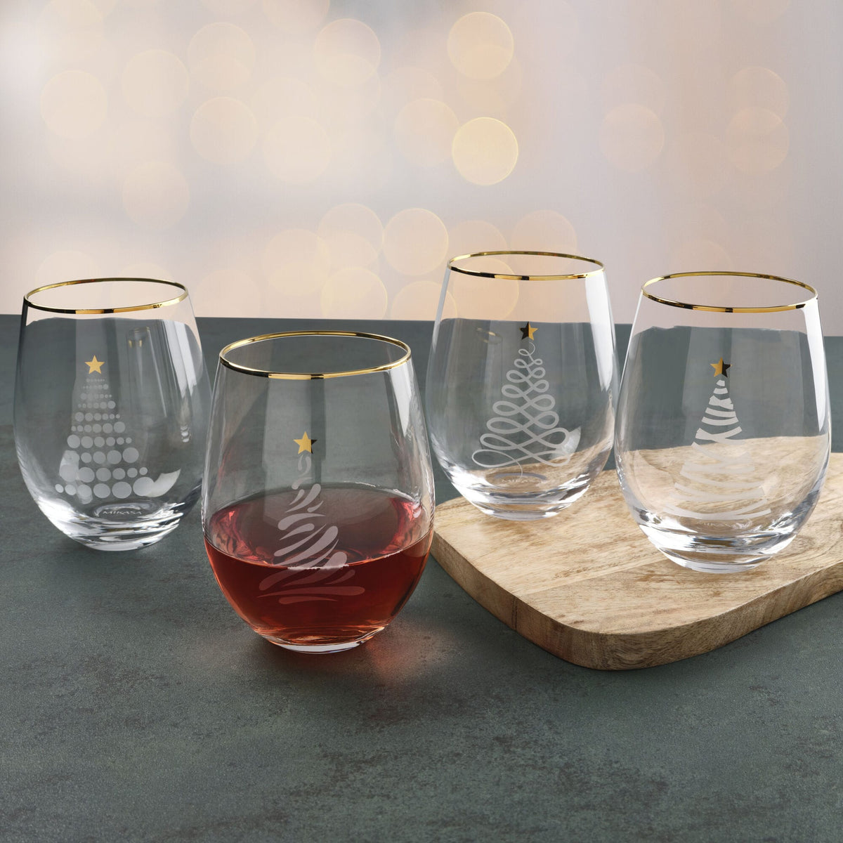 Set of four clear stemless wine glasses with gold rims and white Christmas tree and star designs