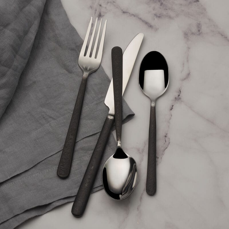 Calyx Black Forged flatware pieces arranged on a gray napkin over a marble surface.
