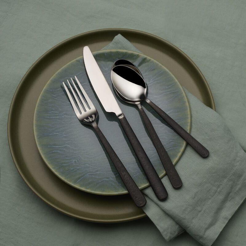 Calyx Black forged flatware arranged on a green plate with a matching napkin