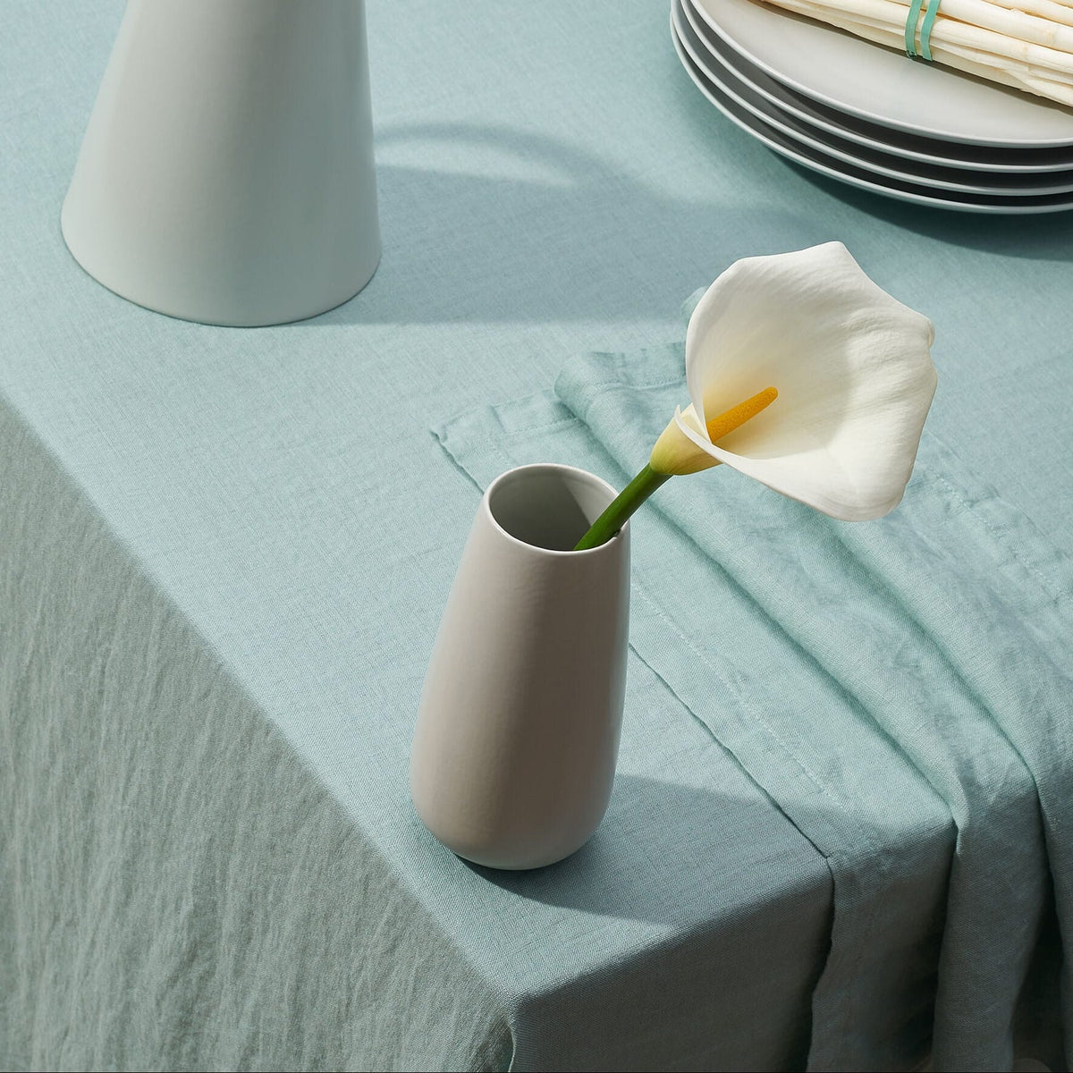 Palm Green European Linen tablecloth on a table with stacked plates and a white calla lily in a vase