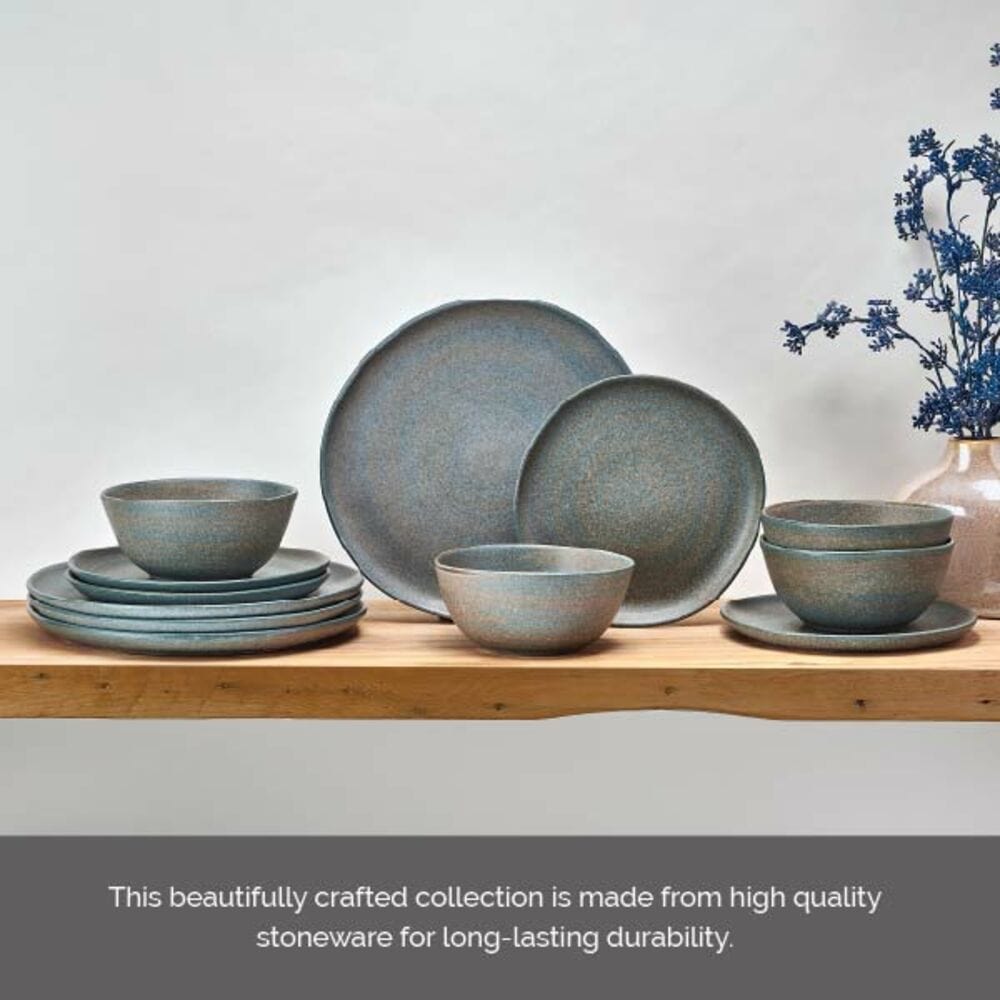 Blue gray stoneware dinnerware arranged on a wooden table with stacked plates bowls and a vase of blue flowers