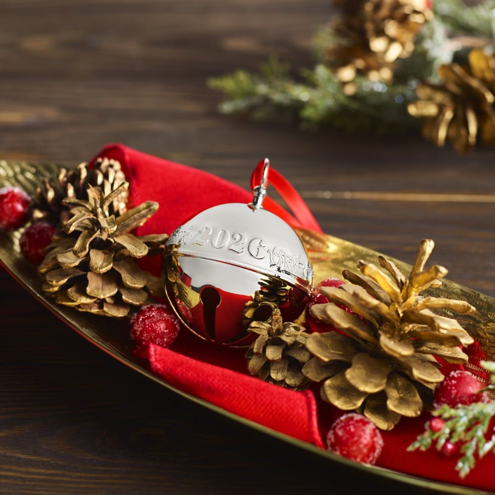 Wallace 2026 Silver Plated Sleigh Bell Ornament nestled in a holiday centerpiece on a gold plate with pinecones red berries and a red napkin.