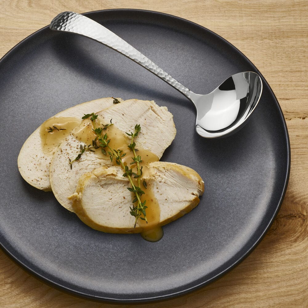 Sliced roasted chicken with thyme on a dark plate, with hammered knife and spoon.