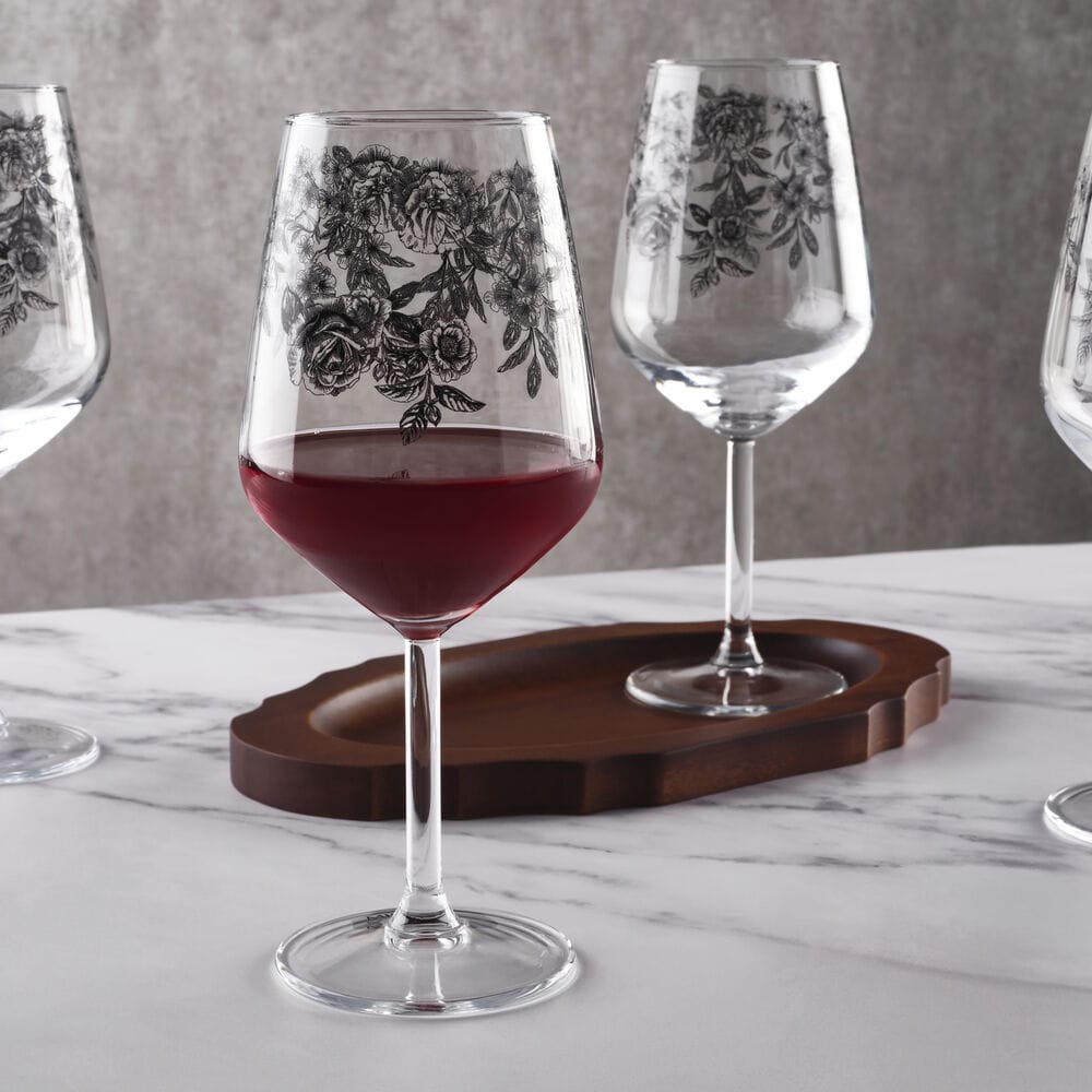 Four Windsor Rose wine glasses arranged on a marble table, one glass filled with red wine