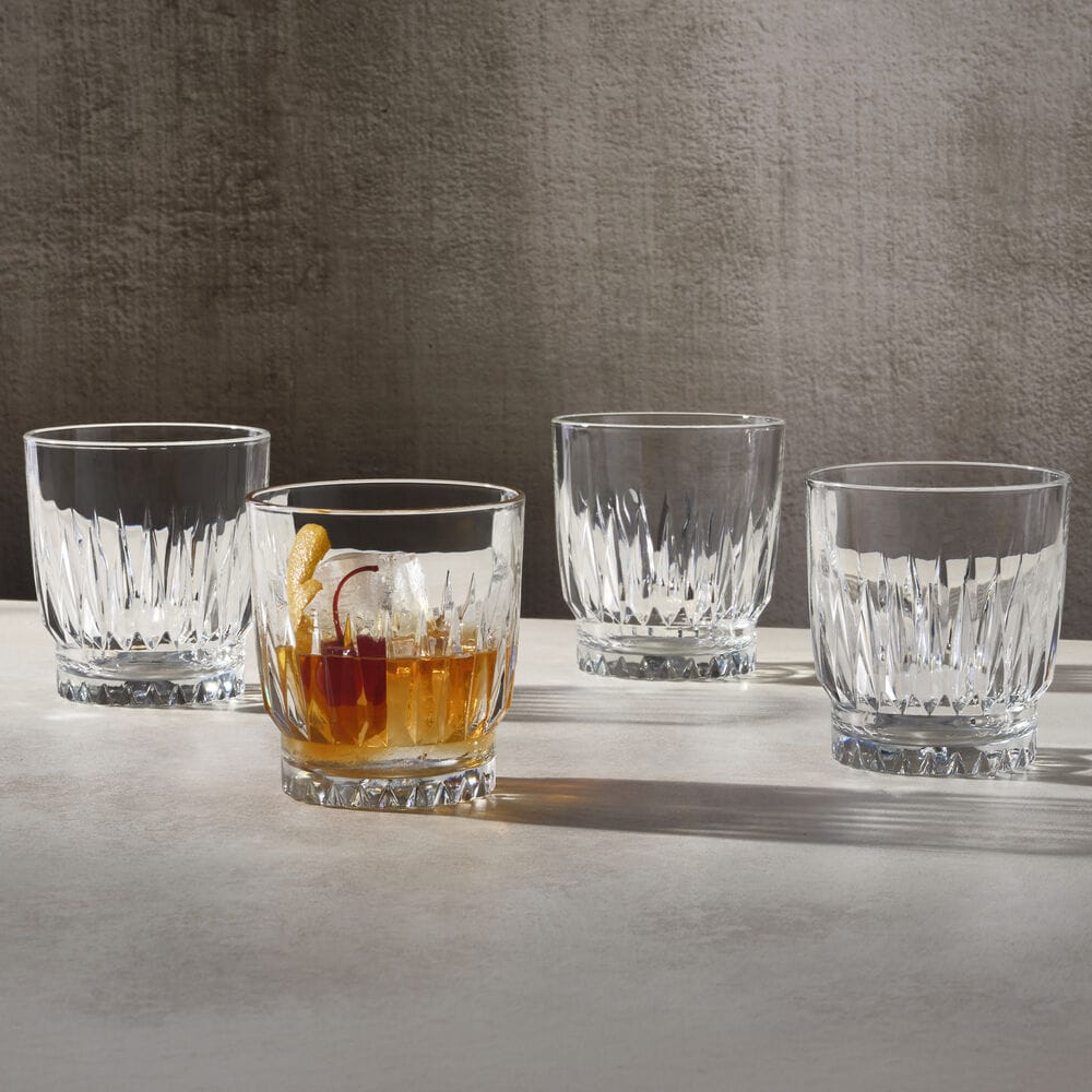 Hampshire four crystal double old fashioned glasses on a light surface with one glass filled with whiskey and lemon twist