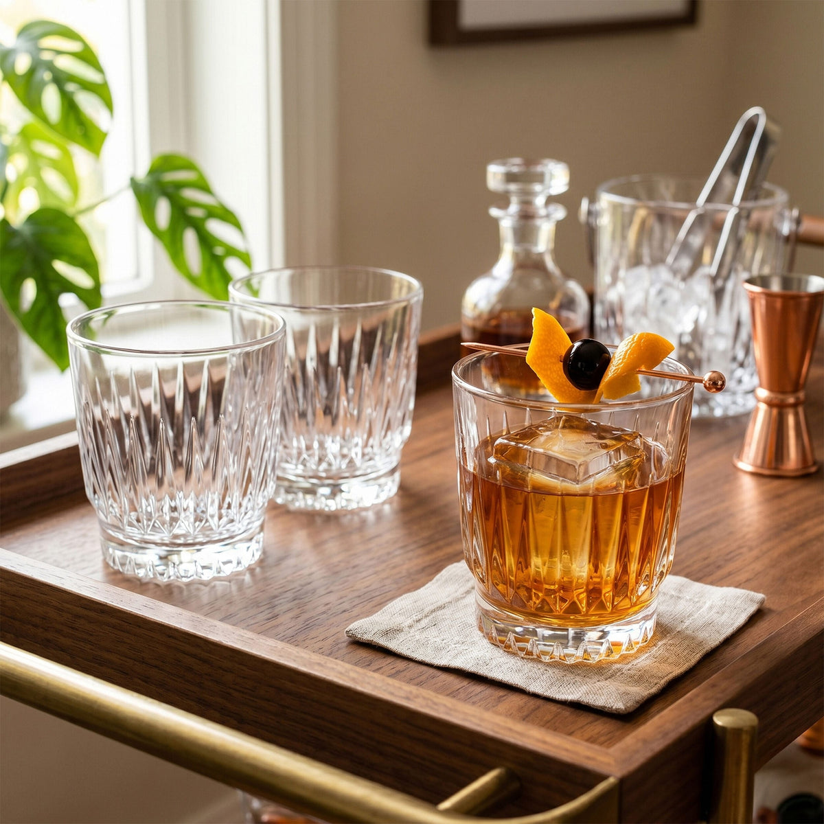 Amber drink with ice in a Hampshire crystal double old fashioned glass with orange twist garnish on a wooden tray