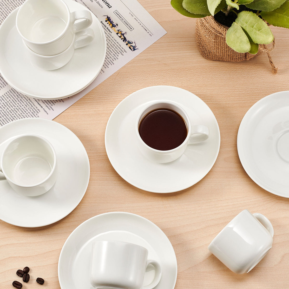 Six white espresso cups with matching saucers arranged on a wooden table.