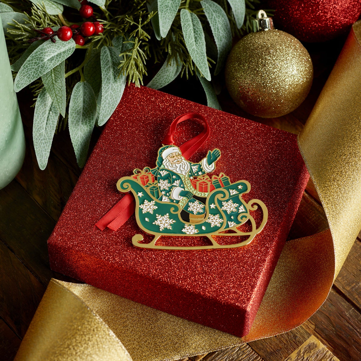 Fitz & Floyd Santa ornament resting on a red glitter gift box with greenery and gold ribbon.