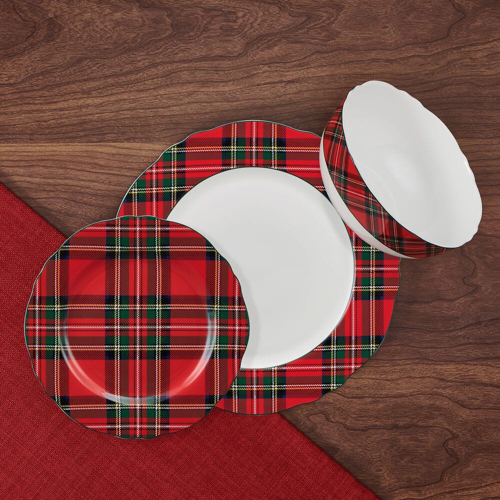 Top down view of tartan red scallop plates and bowls with plaid edges on a wood surface.