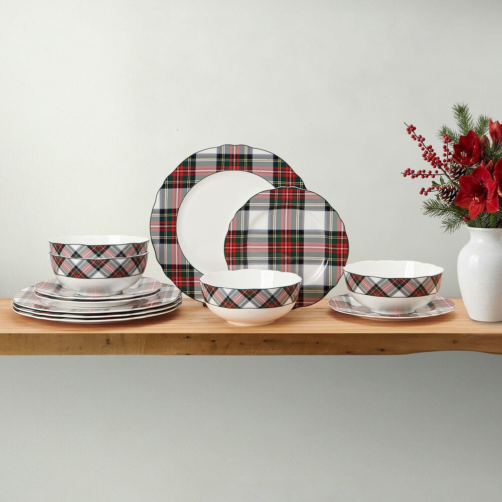 Assorted tartan plaid rim dinnerware pieces including plates and bowls on a wooden shelf with a vase nearby.