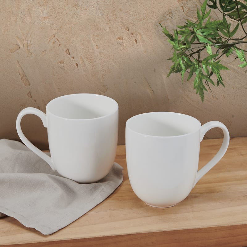 Two white Delray oversized mugs on a wooden surface with a plant in the background.