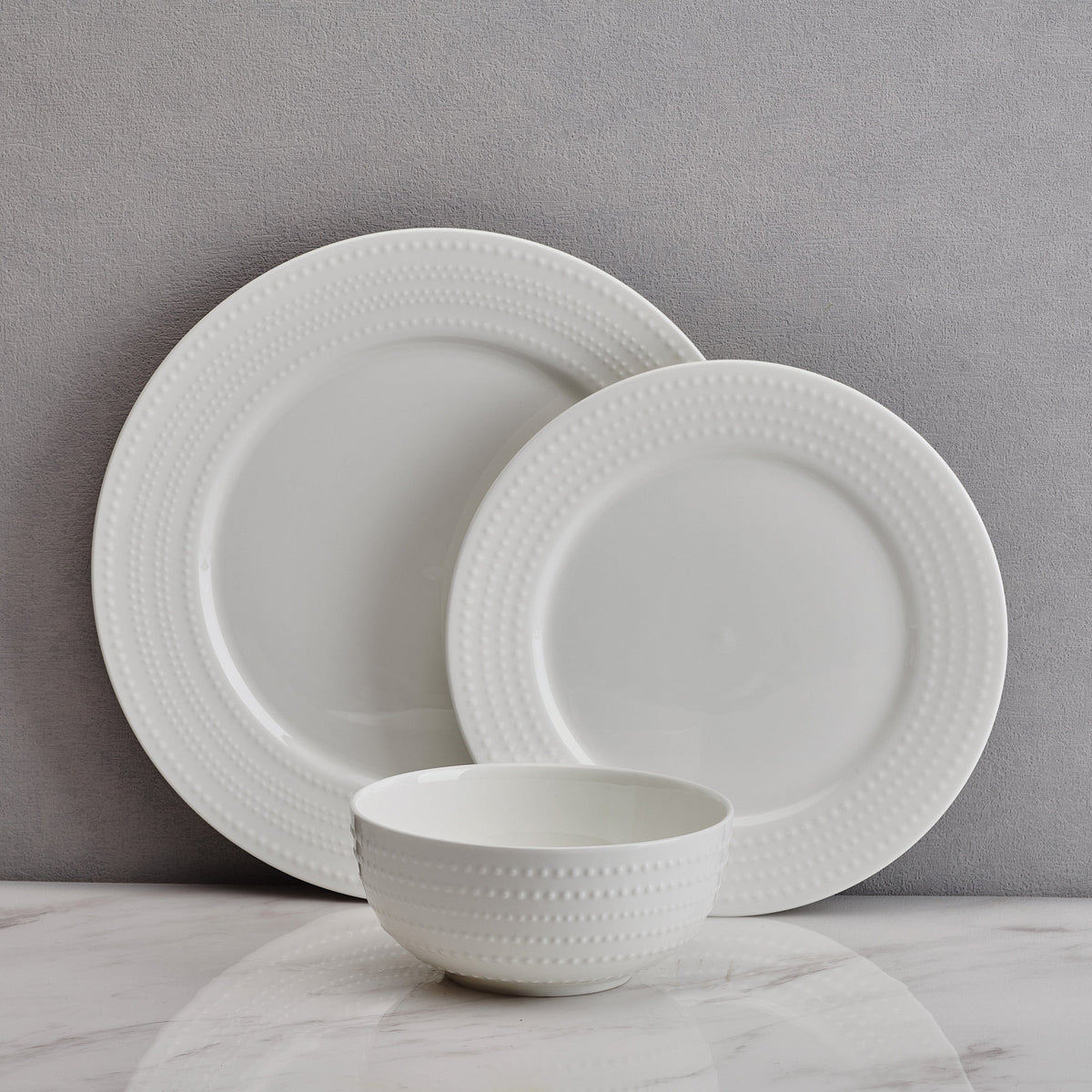 Partial view of the Nellie set of 4 white bowls with dotted beaded rims on a gray surface