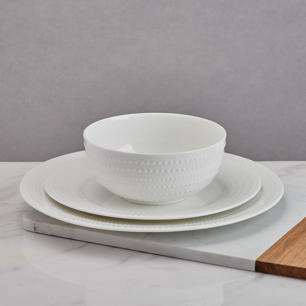 Close up of stacked Nellie white salad plates with dotted rims on a gray backdrop