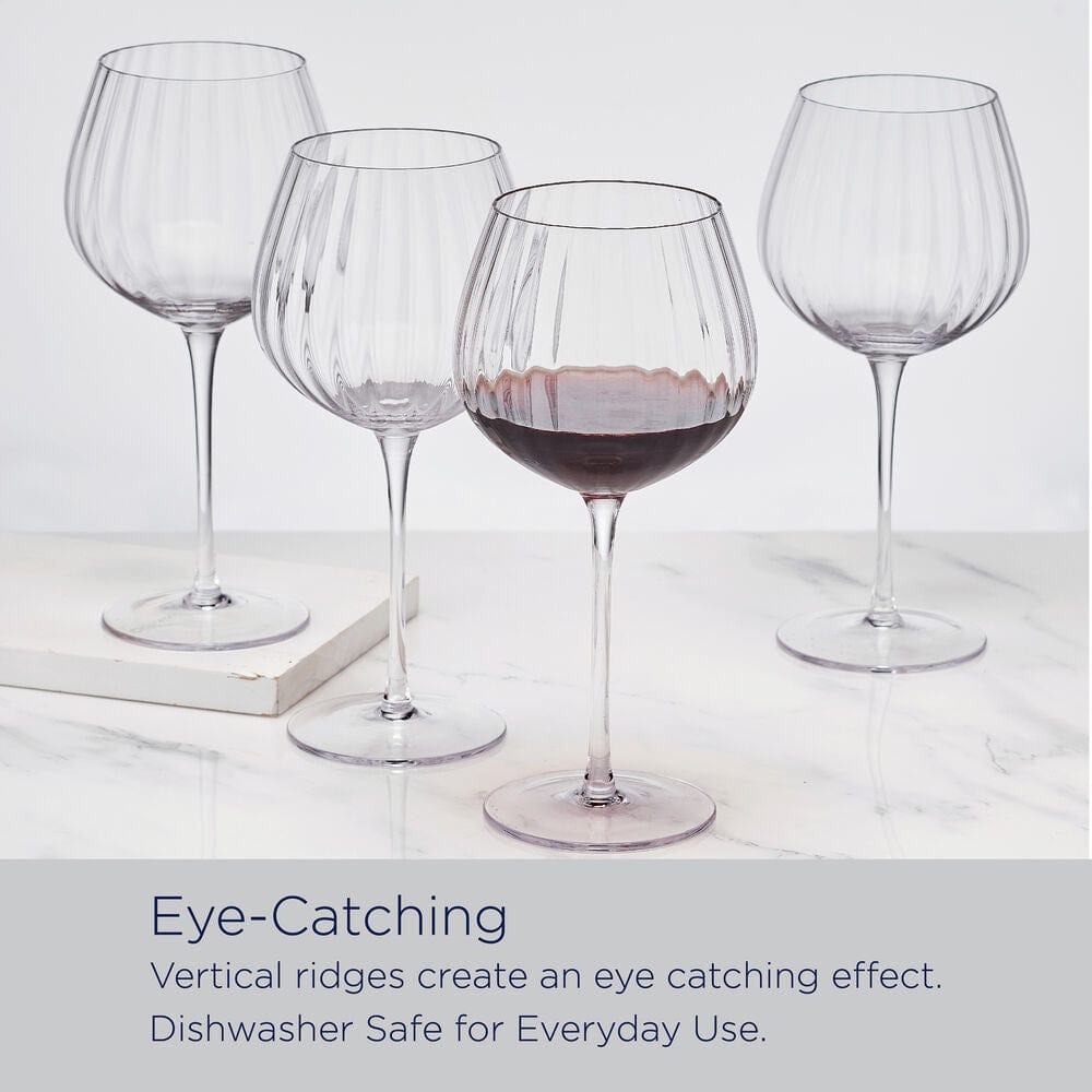 Four optic wine glasses on a marble surface with one glass partially filled with red wine.