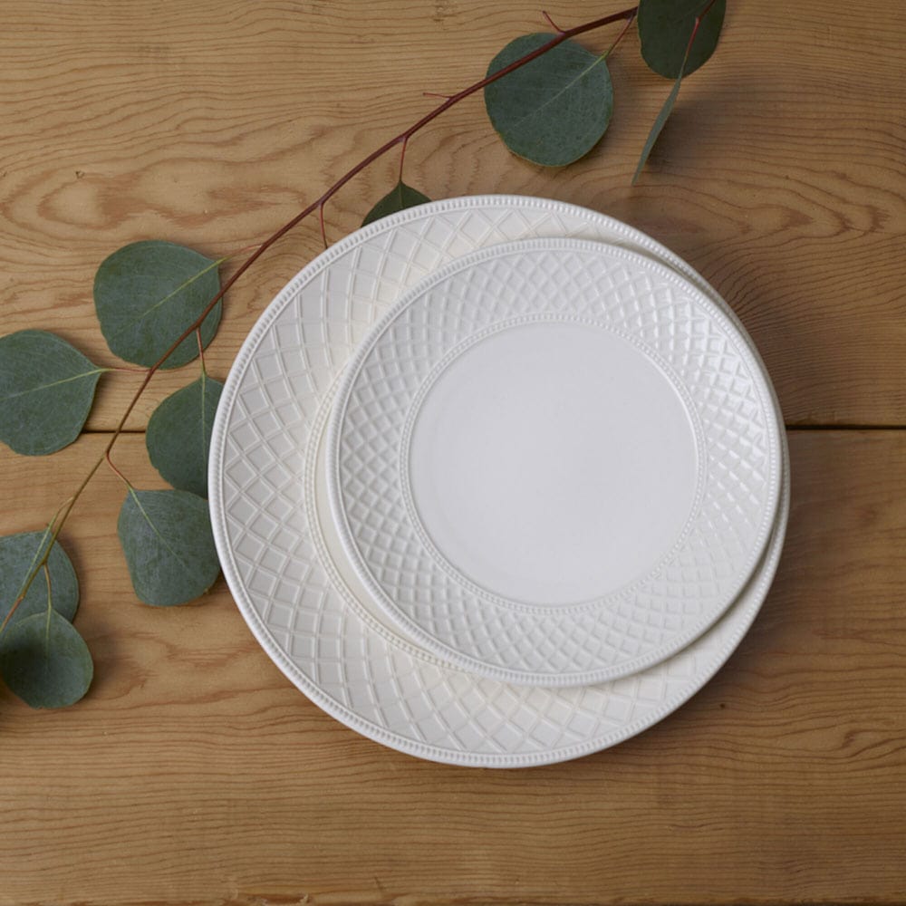 Two white Napa Countryside salad plates stacked on a wooden surface with a eucalyptus sprig