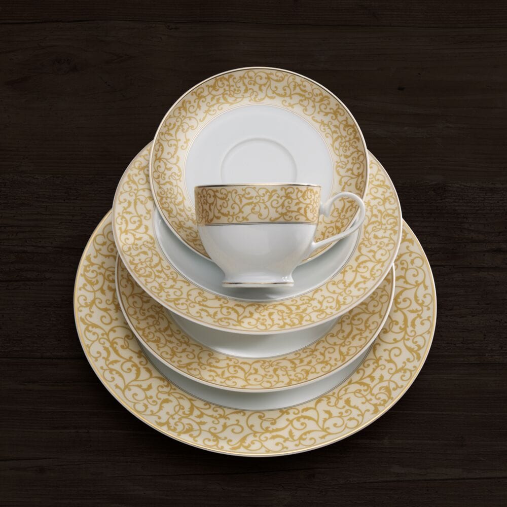Top view of a stack of Parchment Gold bordered plates with a matching teacup and saucer on a dark wooden table.