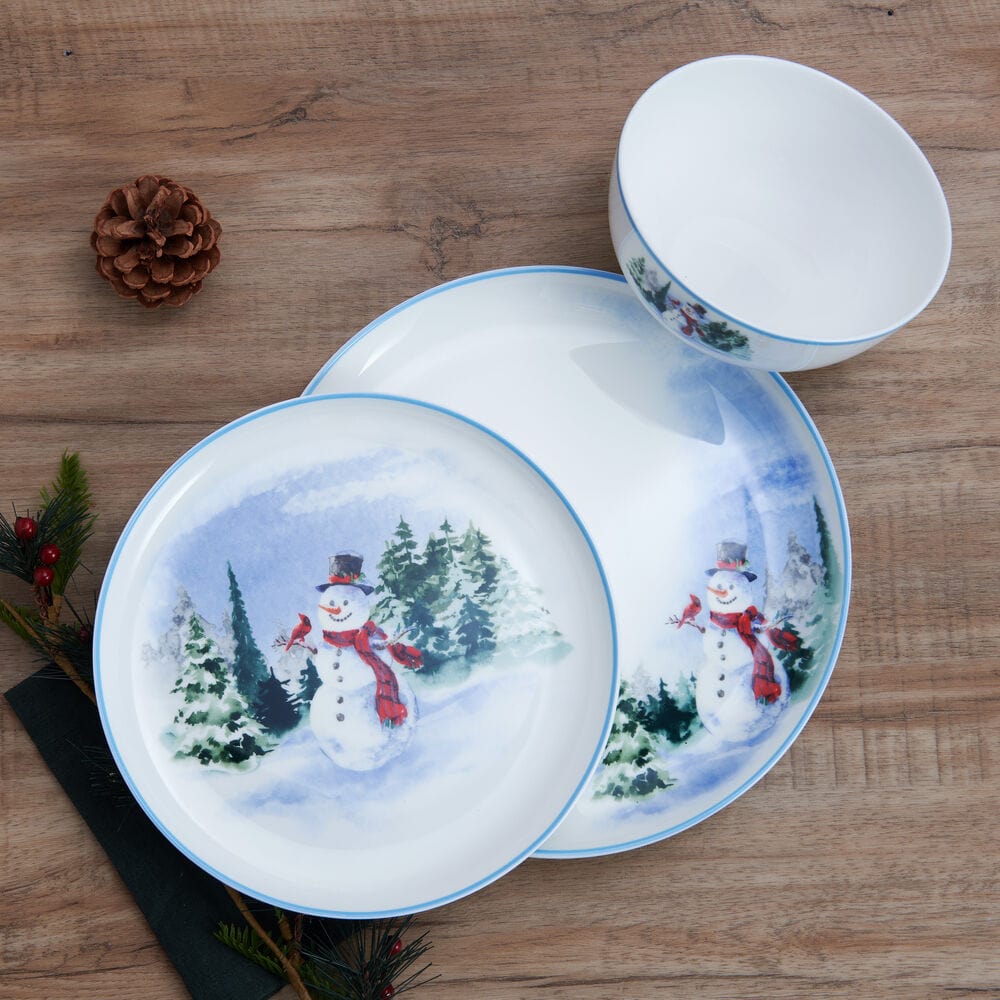 Flat lay of Snowman Forest dinnerware showing plates and bowls with snowman scene arranged on a wooden table