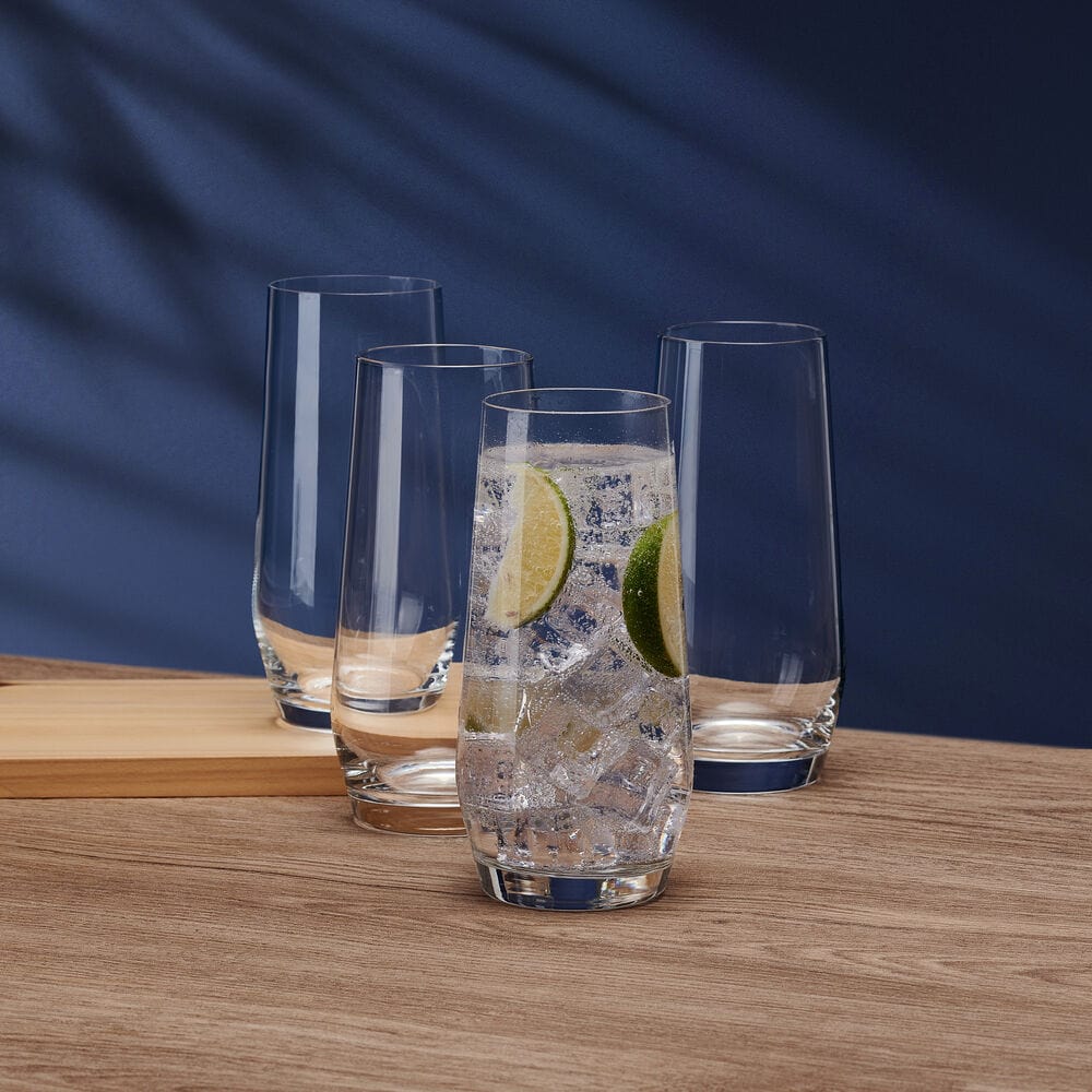 Four tall highball glasses on a wooden surface with the front glass filled with ice and lime wedges