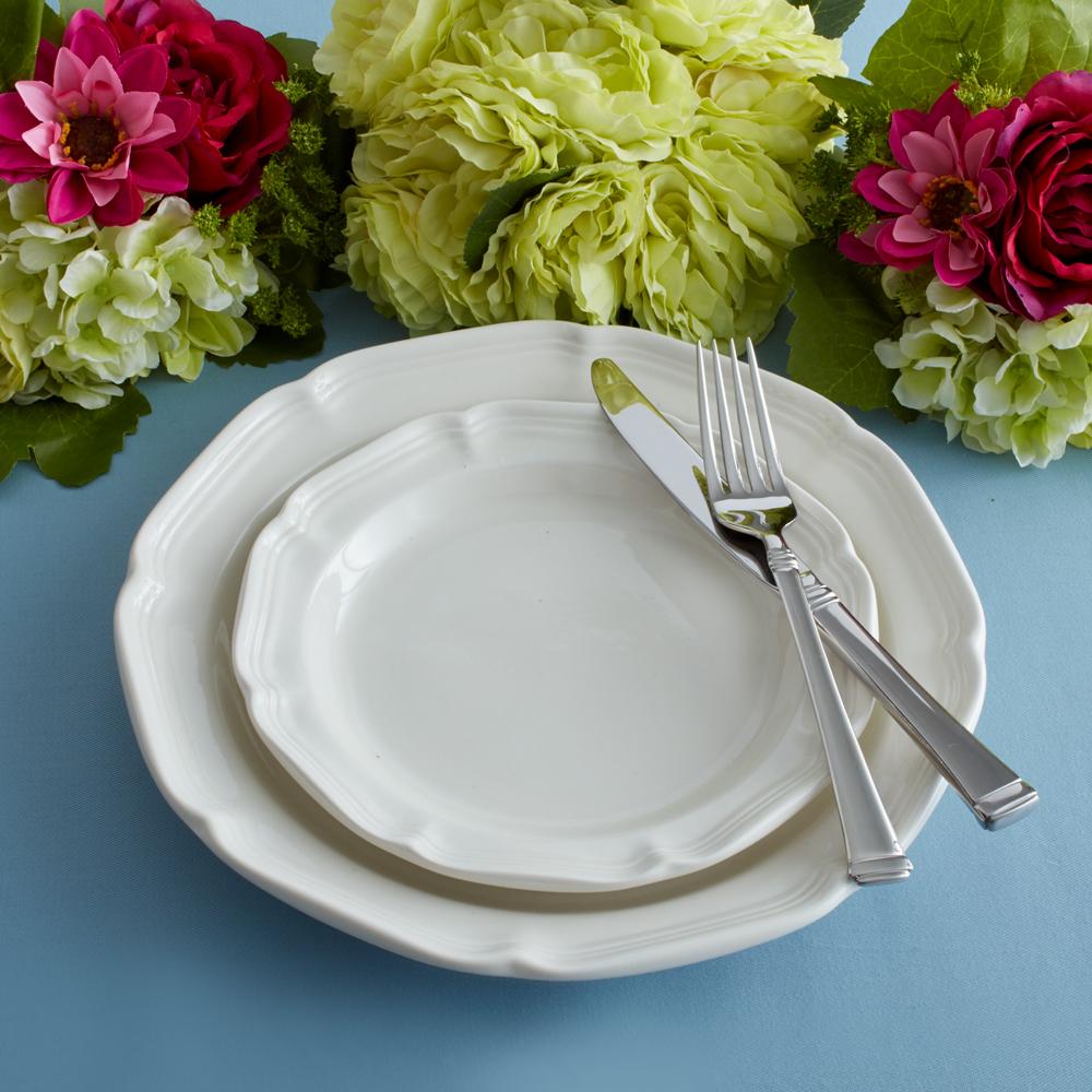 White dinner plates stacked on a blue table with a knife and fork and colorful flowers in the background